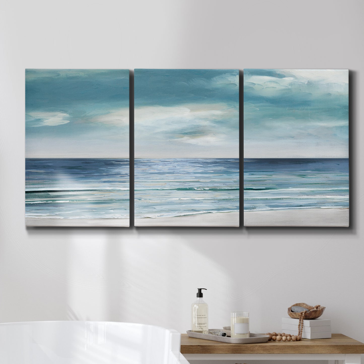 Three-panel canvas wall art featuring calm coastal shoreline, displayed in a bathroom above a bathtub.
