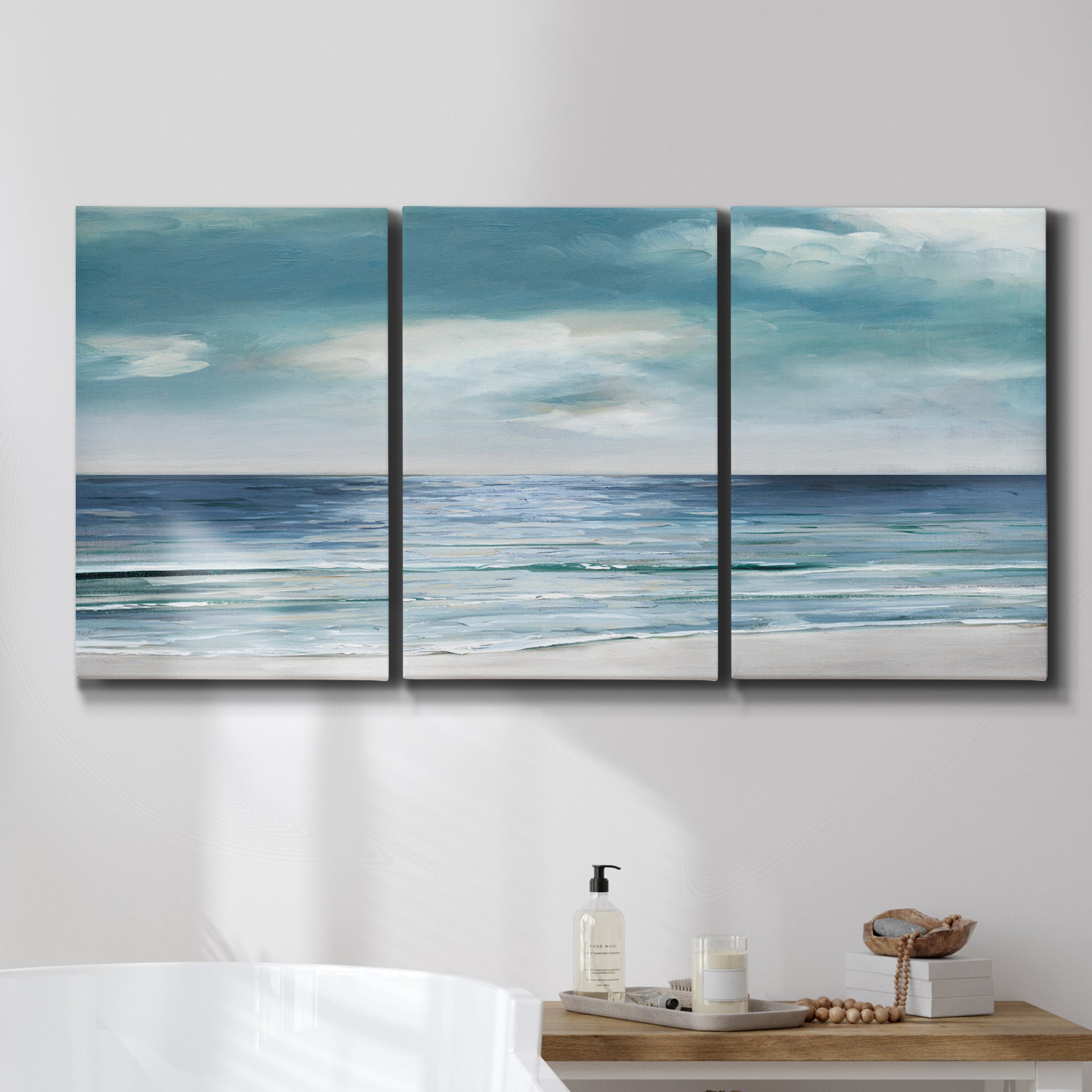 Three-panel canvas wall art featuring calm coastal shoreline, displayed in a bathroom above a bathtub.