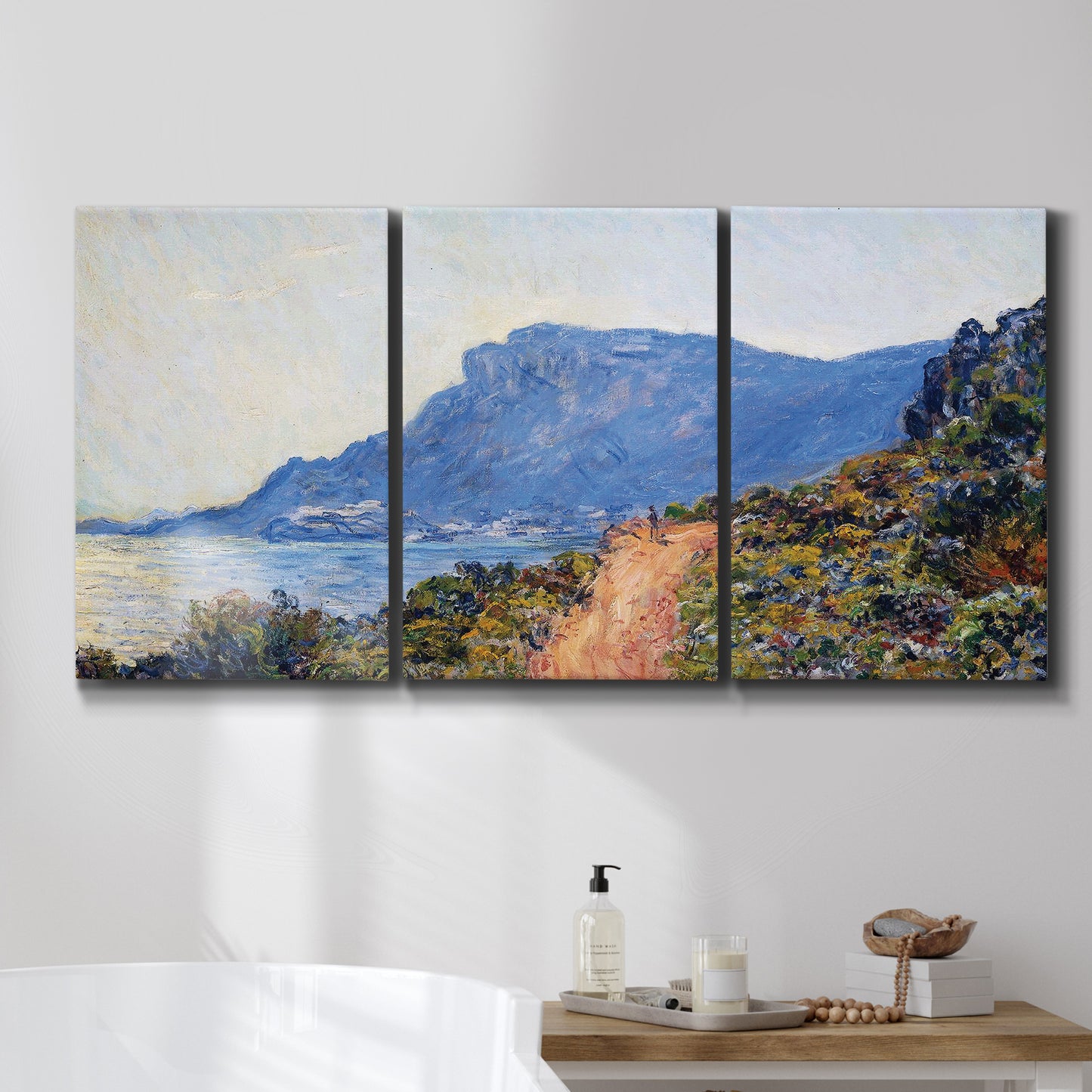 Three-panel canvas wall art featuring winding coastal road above sea, displayed in a bathroom above a bathtub.