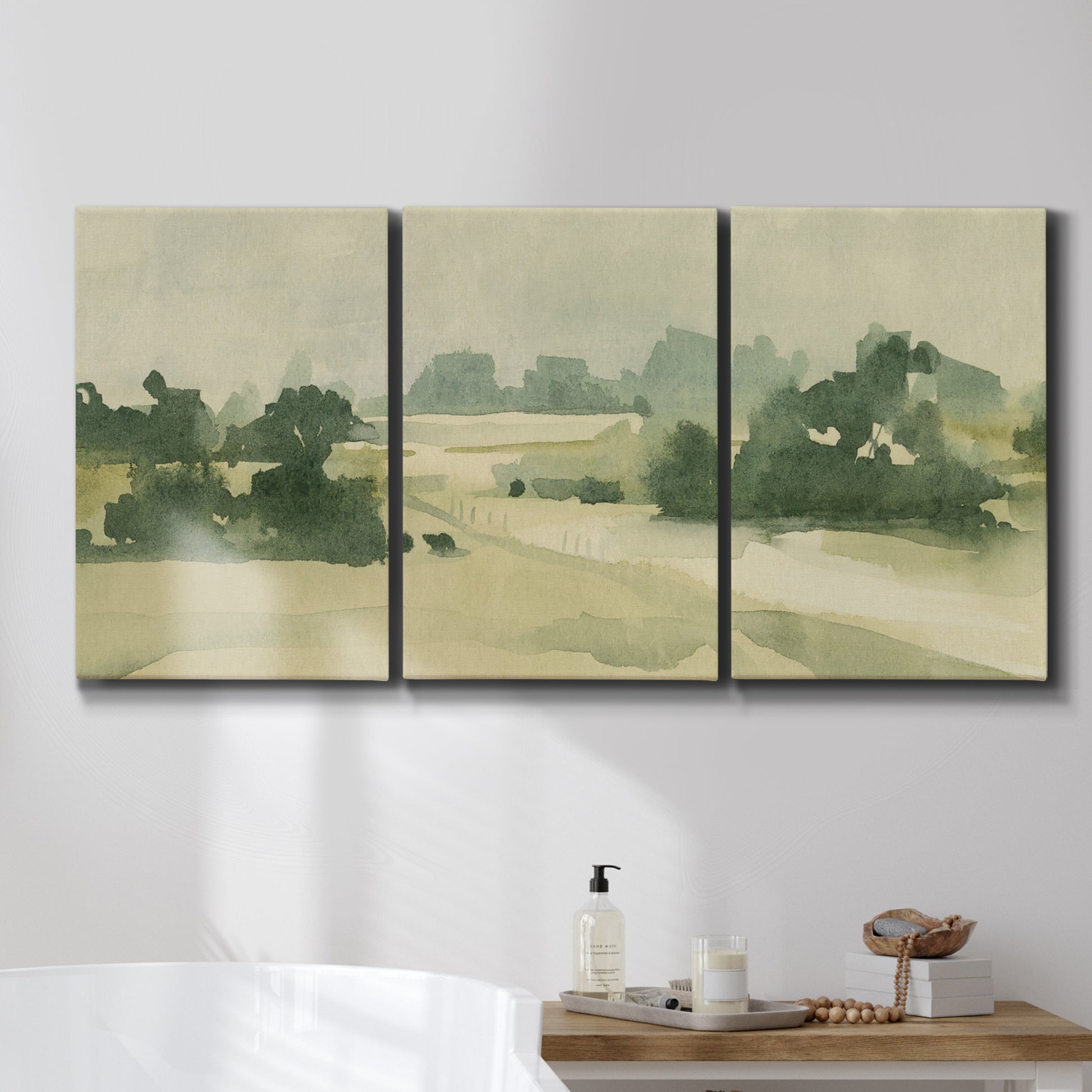 Three-panel canvas wall art featuring pasture landscape in soft watercolor, displayed in a bathroom above a bathtub.