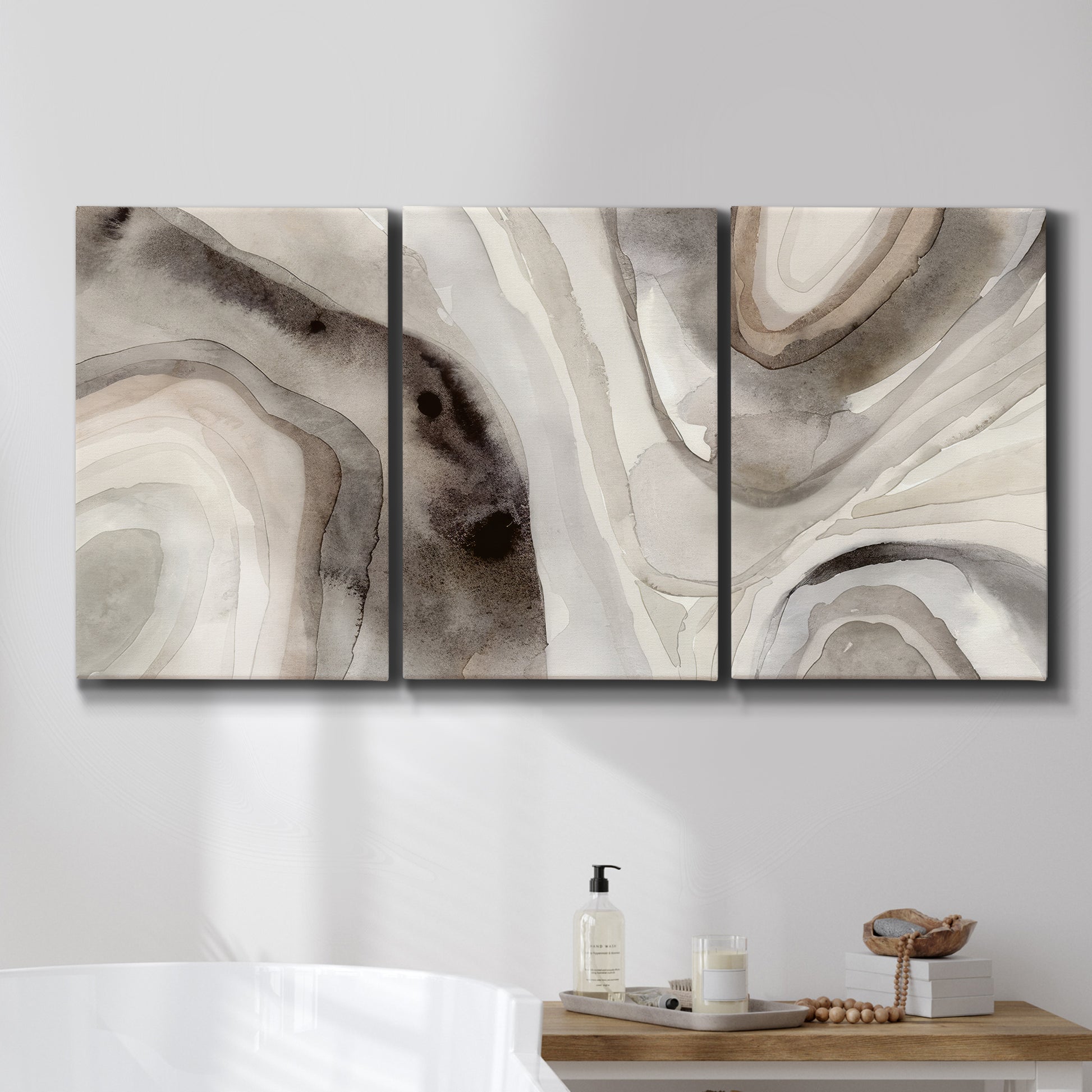 Three-panel canvas wall art featuring layered stone inspired abstract forms, displayed in a bathroom above a bathtub.