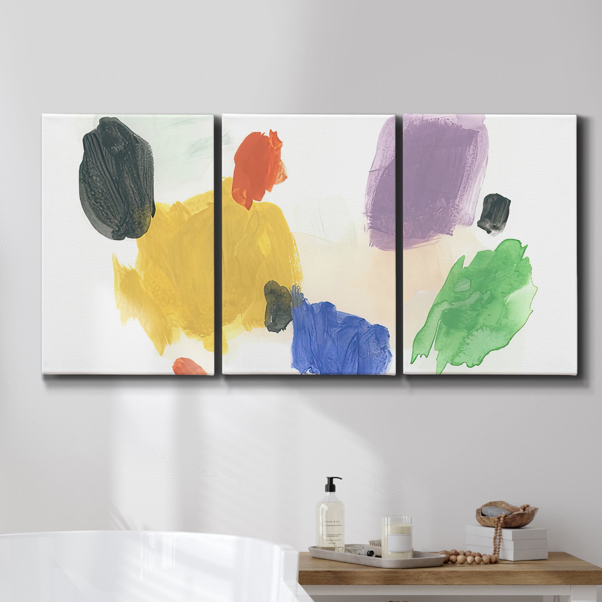 Three-panel canvas wall art featuring inkblot style abstract color symmetry, displayed in a bathroom above a bathtub.