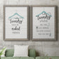 Set of two gray barnwood framed canvas prints depicting a coordinated art pair of humorous laundry-room sayings and clothing icons rendered as rustic typographic wall art above a sofa in a modern living room.