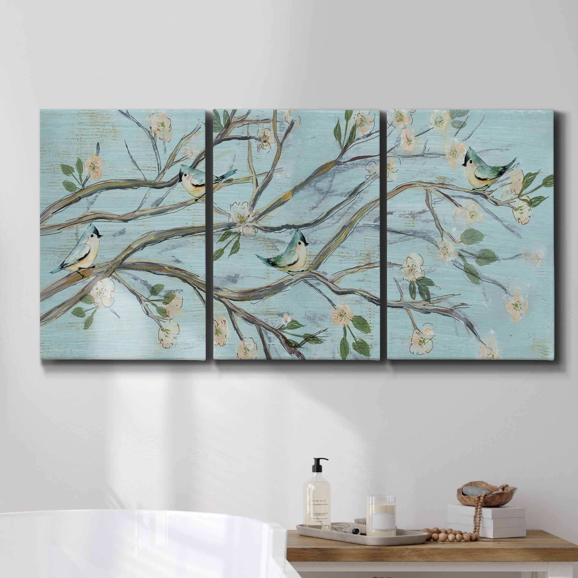 Three-panel canvas wall art featuring blue sky with flowering branches, displayed in a bathroom above a bathtub.