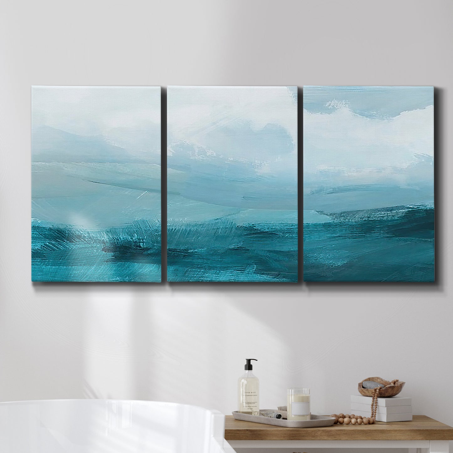 Three-panel canvas wall art featuring vertical coastal elements with rising light, displayed in a bathroom above a bathtub.