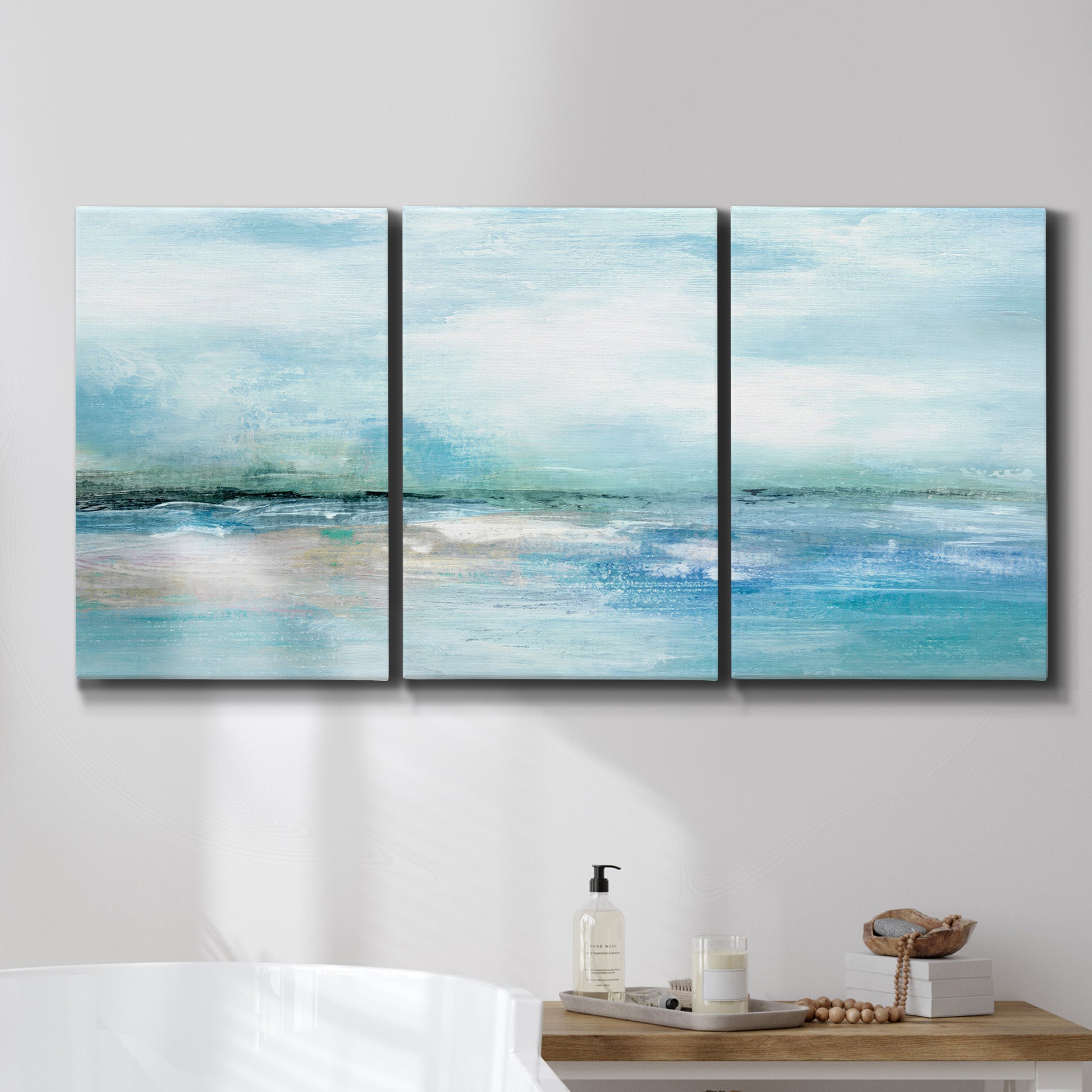 Three-panel canvas wall art featuring sunset silhouette over coastal water, displayed in a bathroom above a bathtub.