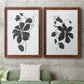 Set of two maple barnwood framed canvas prints depicting a coordinated art pair of black leafy vine silhouettes rendered as minimalist botanical prints above a sofa in a modern living room.