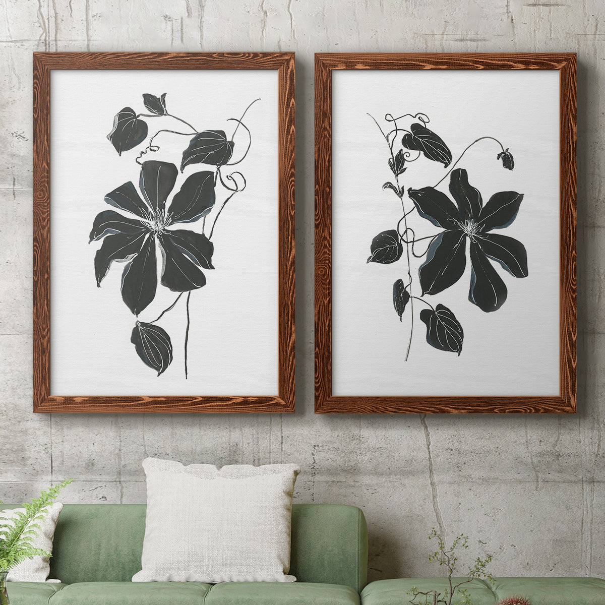 Set of two maple barnwood framed canvas prints depicting a coordinated art pair of black leafy vine silhouettes rendered as minimalist botanical prints above a sofa in a modern living room.