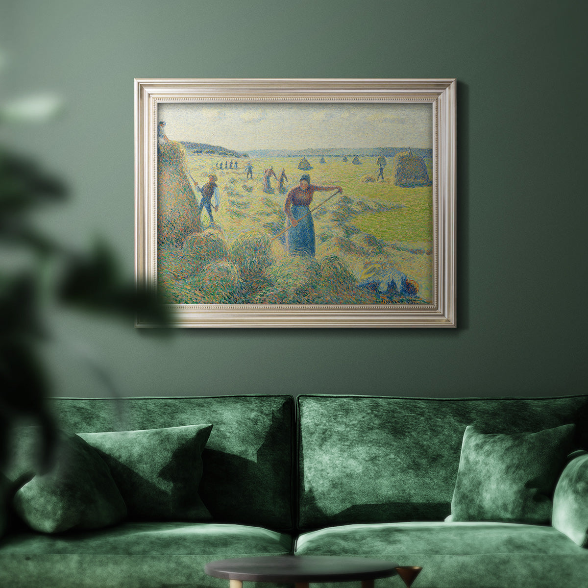 Impressionist rural hay harvest landscape by Camille Pissarro in an ornate champagne frame displayed in a dark-toned interior setting.