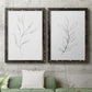 Set of two black barnwood framed canvas prints depicting a coordinated art pair of single continuous-line leafy branches rendered as minimalist botanical line drawings above a sofa in a modern living room.