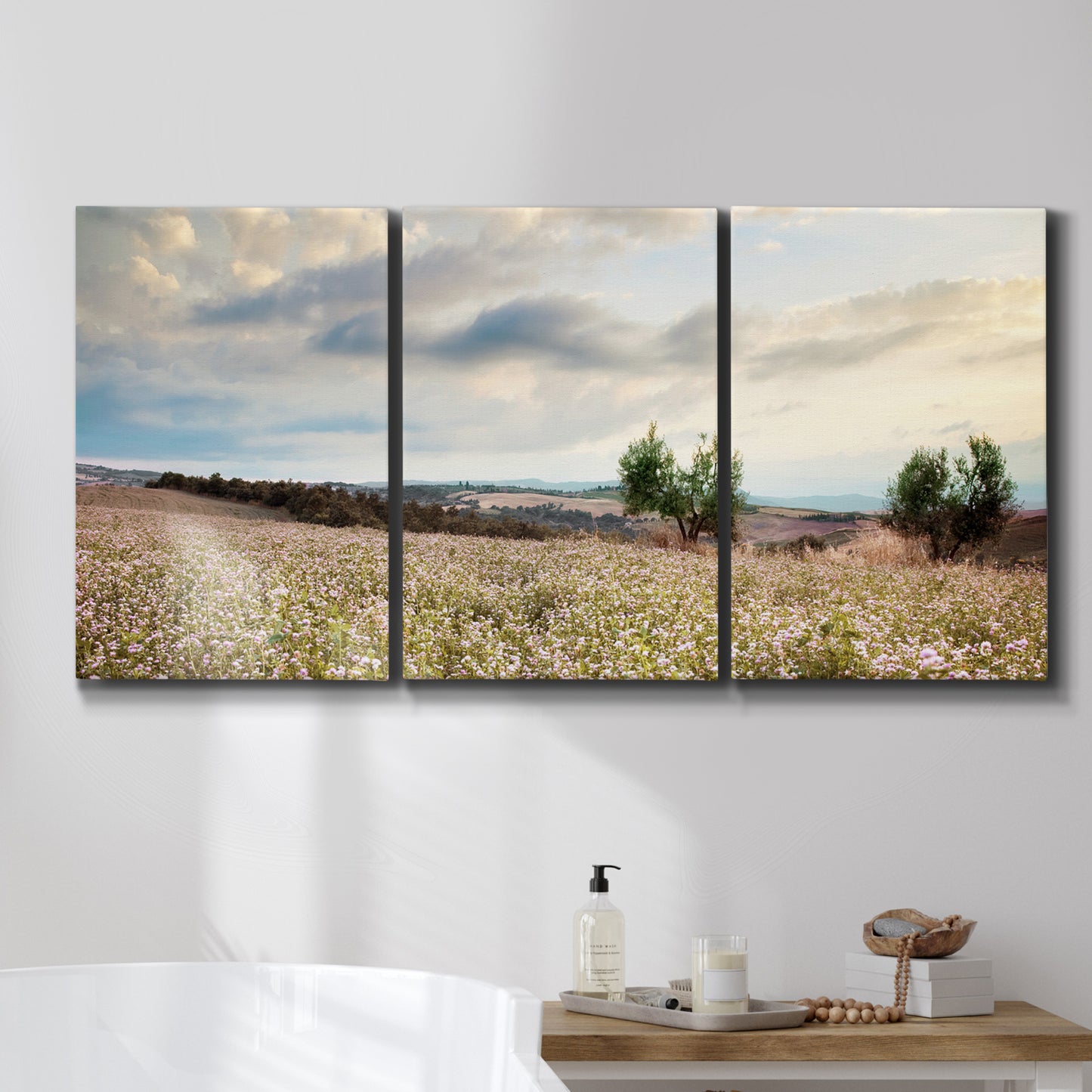Three-panel canvas wall art featuring wildflowers across tuscan landscape, displayed in a bathroom above a bathtub.