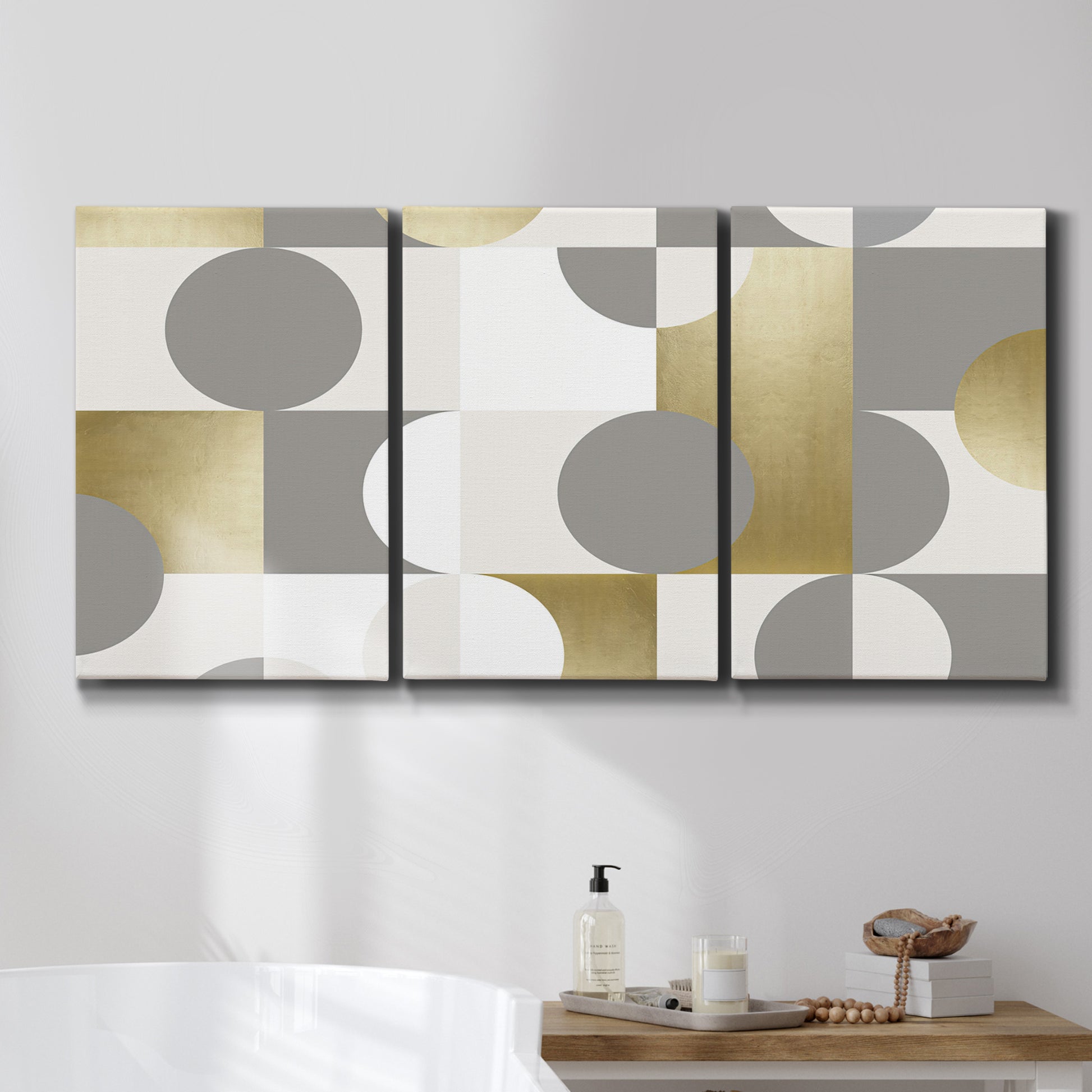 Three-panel canvas wall art featuring geometric gold abstract reflections, displayed in a bathroom above a bathtub.