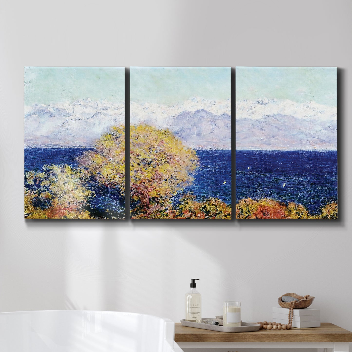 Three-panel canvas wall art featuring mediterranean coastline with headland, displayed in a bathroom above a bathtub.