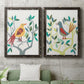 Set of two black barnwood framed canvas prints depicting a coordinated art pair of stylized colorful birds perched among leafy branches rendered as modern folk-art bird illustrations above a sofa in a modern living room.