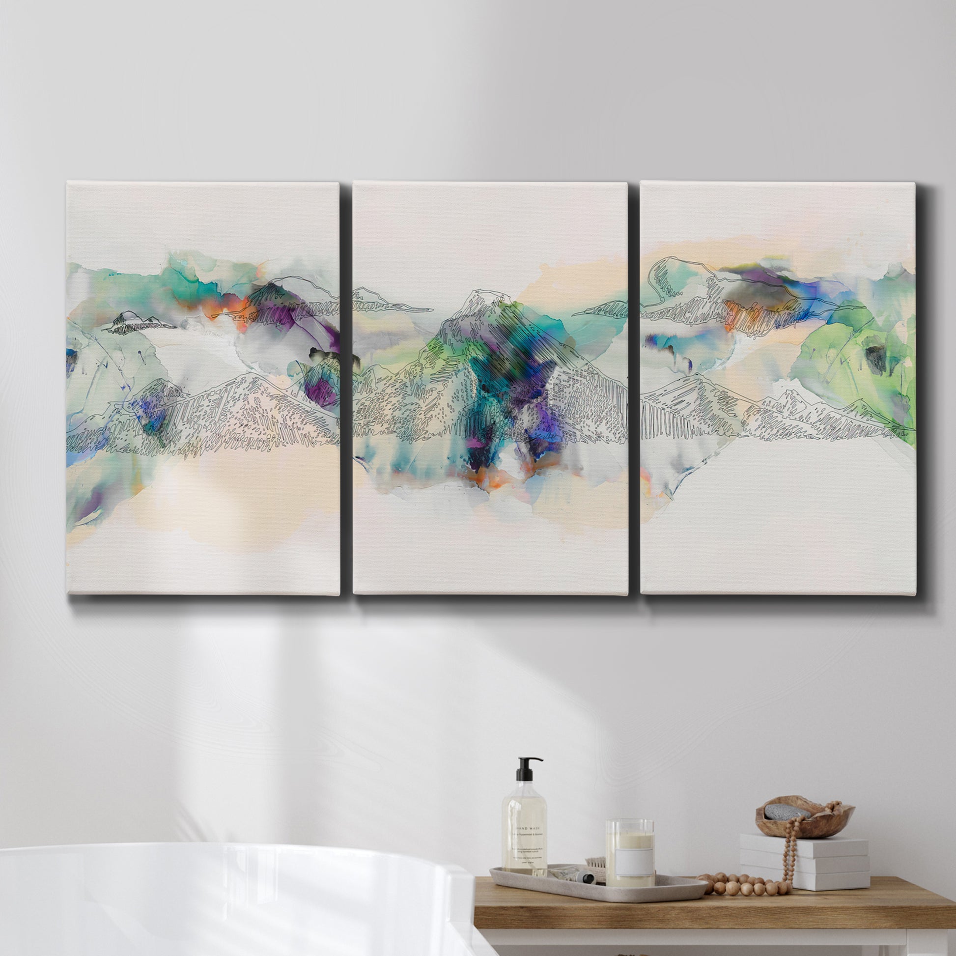 Three-panel canvas wall art featuring abstract mountain range watercolor, displayed in a bathroom above a bathtub.
