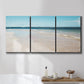 Three-panel canvas wall art featuring white sand beach with gentle waves, displayed in a bathroom above a bathtub.
