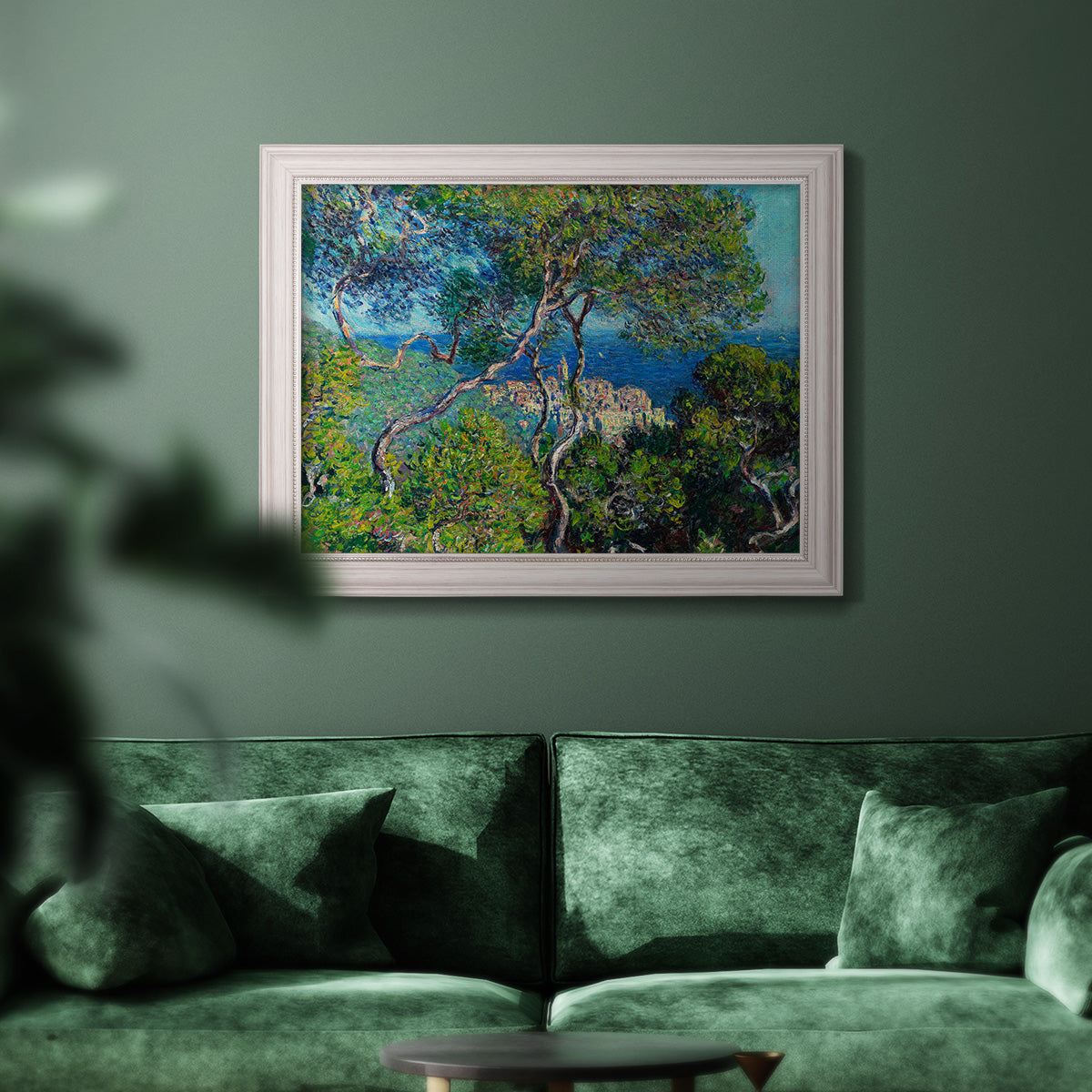 Impressionist Mediterranean coastal landscape by Claude Monet in an ornate weathered white frame displayed in a dark-toned interior setting.