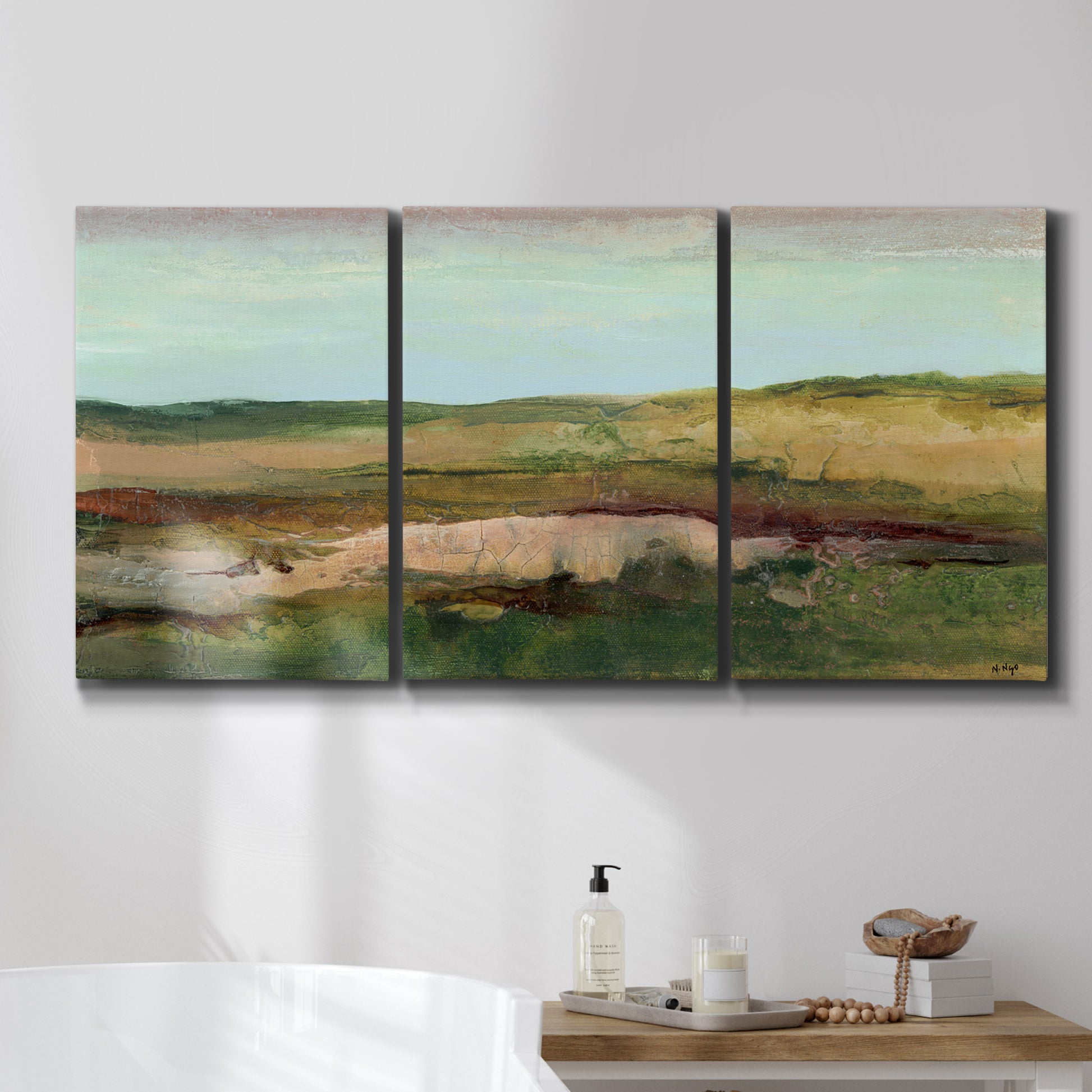 Three-panel canvas wall art featuring pastoral landscape with winding road, displayed in a bathroom above a bathtub.