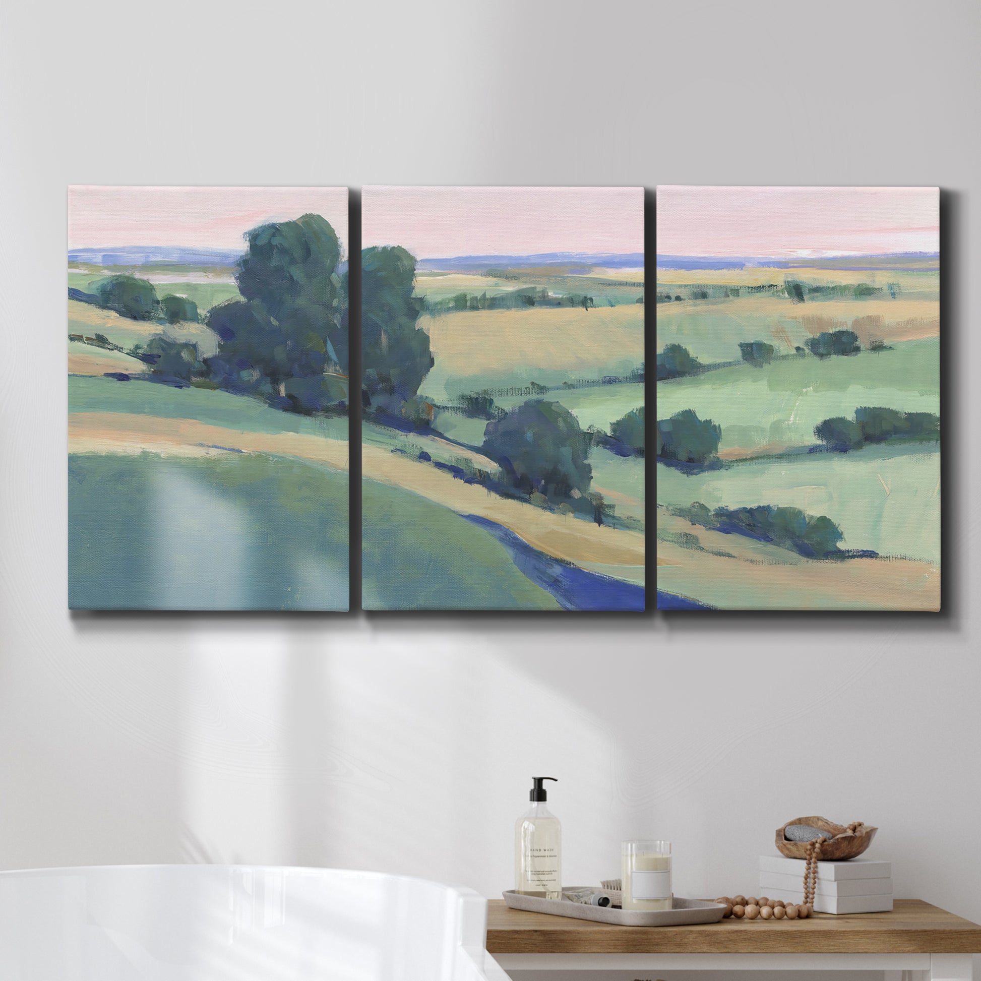 Three-panel canvas wall art featuring pastoral countryside with rocky outcrop, displayed in a bathroom above a bathtub.