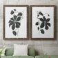 Set of two walnut barnwood framed canvas prints depicting a coordinated art pair of black leafy vine silhouettes rendered as minimalist botanical prints above a sofa in a modern living room.