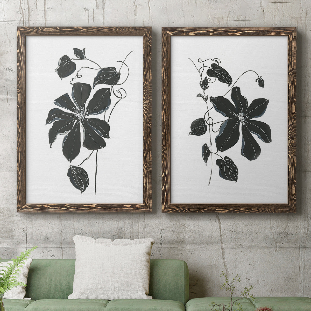 Set of two walnut barnwood framed canvas prints depicting a coordinated art pair of black leafy vine silhouettes rendered as minimalist botanical prints above a sofa in a modern living room.