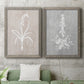 Set of two gray barnwood framed canvas prints depicting a coordinated art pair of white botanical silhouettes on softly weathered neutral backgrounds rendered as rustic minimalist botanical prints above a sofa in a modern living room.