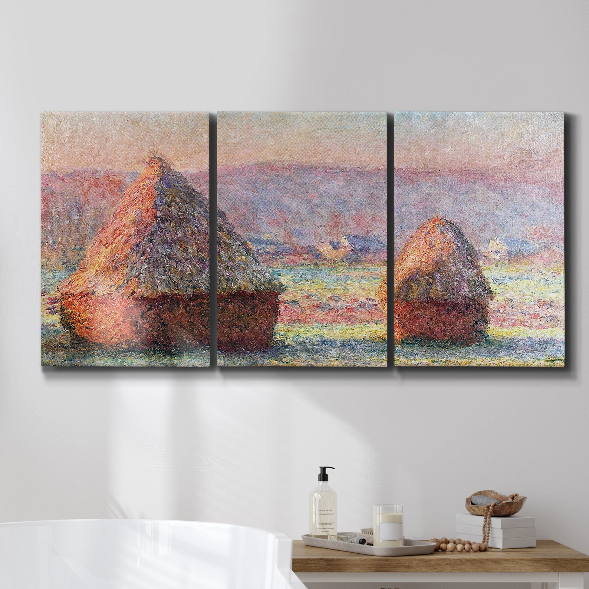Three-panel canvas wall art featuring winter grainstacks glowing at sunset, displayed in a bathroom above a bathtub.