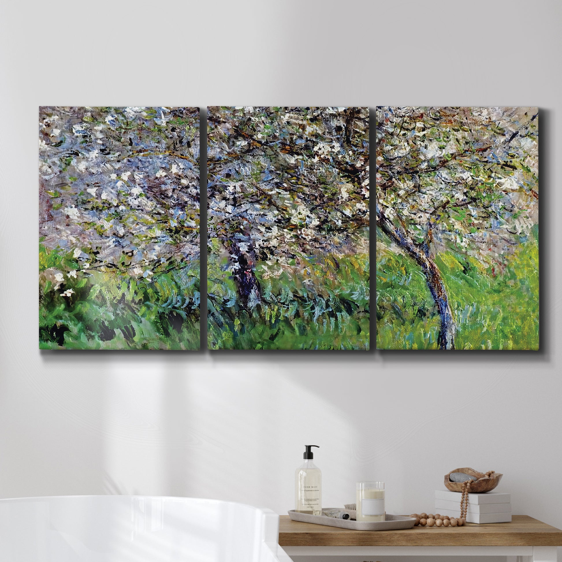 Three-panel canvas wall art featuring apple trees blooming beside water, displayed in a bathroom above a bathtub.