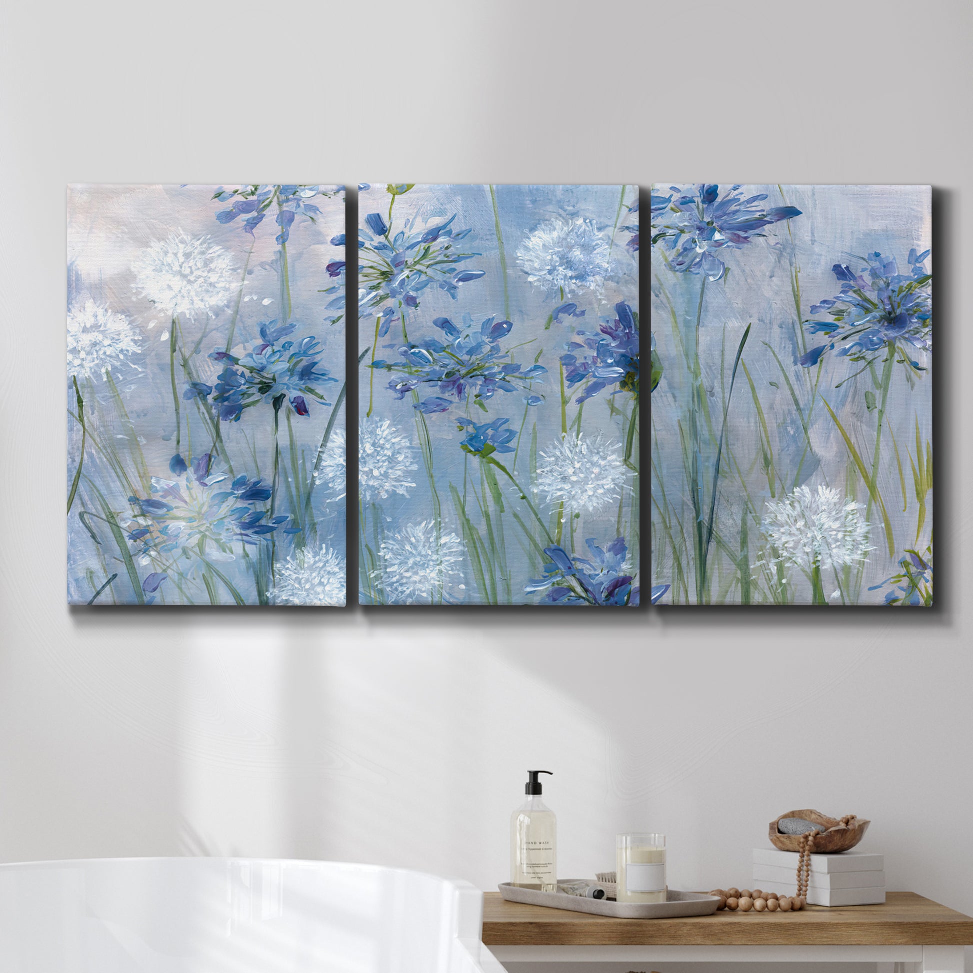 Three-panel canvas wall art featuring delicate watercolor floral blooms, displayed in a bathroom above a bathtub.