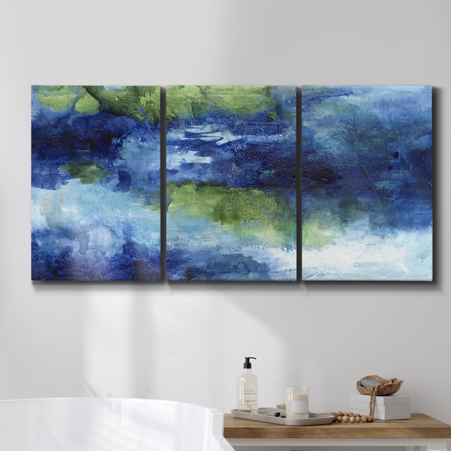 Three-panel canvas wall art featuring flowing blue abstract watercolor, displayed in a bathroom above a bathtub.