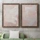 Set of two walnut barnwood framed canvas prints depicting a coordinated art pair of soft blush and white painterly fields rendered as minimalist color-field abstracts above a sofa in a modern living room.