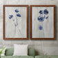 Set of two maple barnwood framed canvas prints depicting a coordinated art pair of blue wildflower stems on weathered neutral paper rendered as rustic monochrome botanical paintings above a sofa in a modern living room.