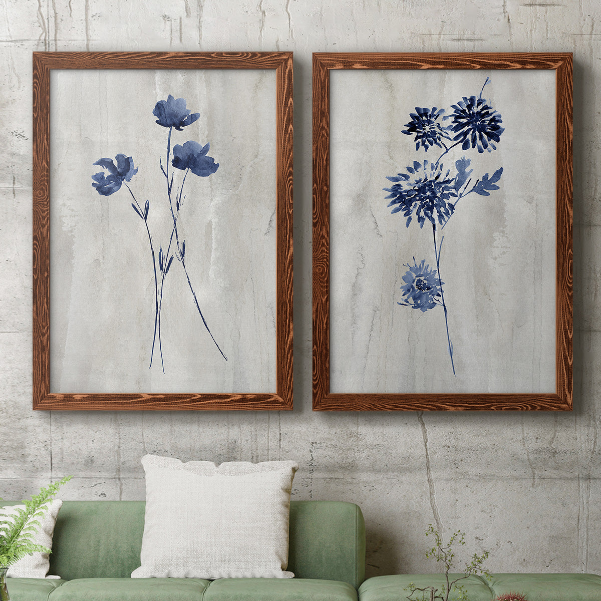 Set of two maple barnwood framed canvas prints depicting a coordinated art pair of blue wildflower stems on weathered neutral paper rendered as rustic monochrome botanical paintings above a sofa in a modern living room.