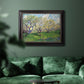 Impressionist spring orchard landscape by Vincent van Gogh in an ornate black frame with gilded inner detail displayed in a dark-toned interior setting.