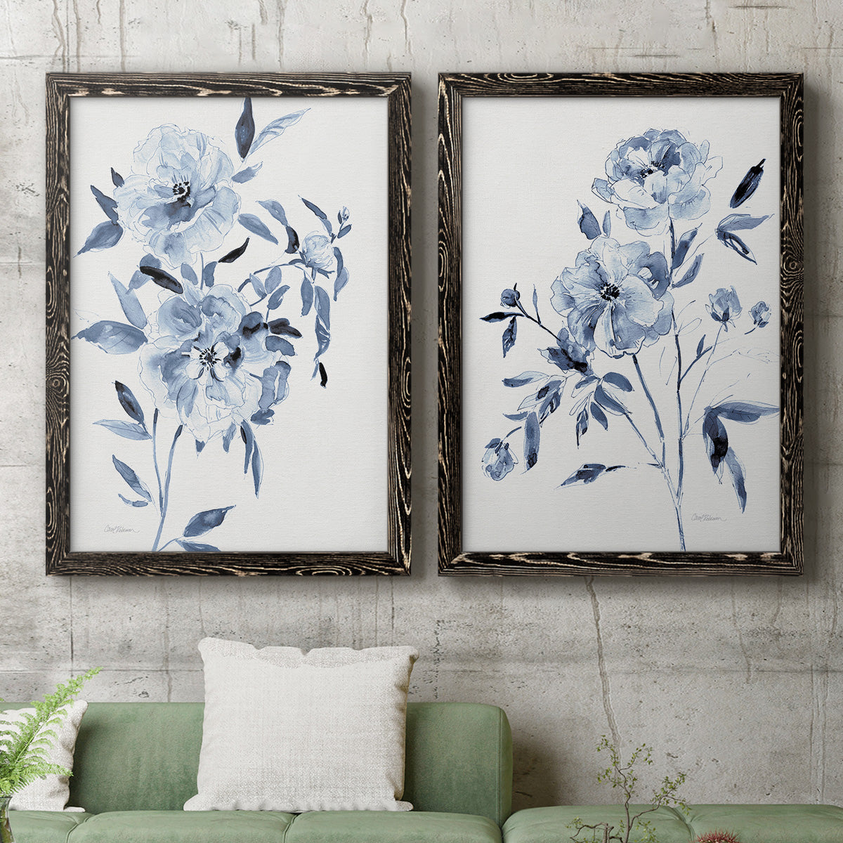 Set of two black barnwood framed canvas prints depicting a coordinated art pair of loose blue flowers and leafy branches rendered as expressive watercolor botanical paintings above a sofa in a modern living room.