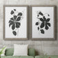Set of two gray barnwood framed canvas prints depicting a coordinated art pair of black leafy vine silhouettes rendered as minimalist botanical prints above a sofa in a modern living room.