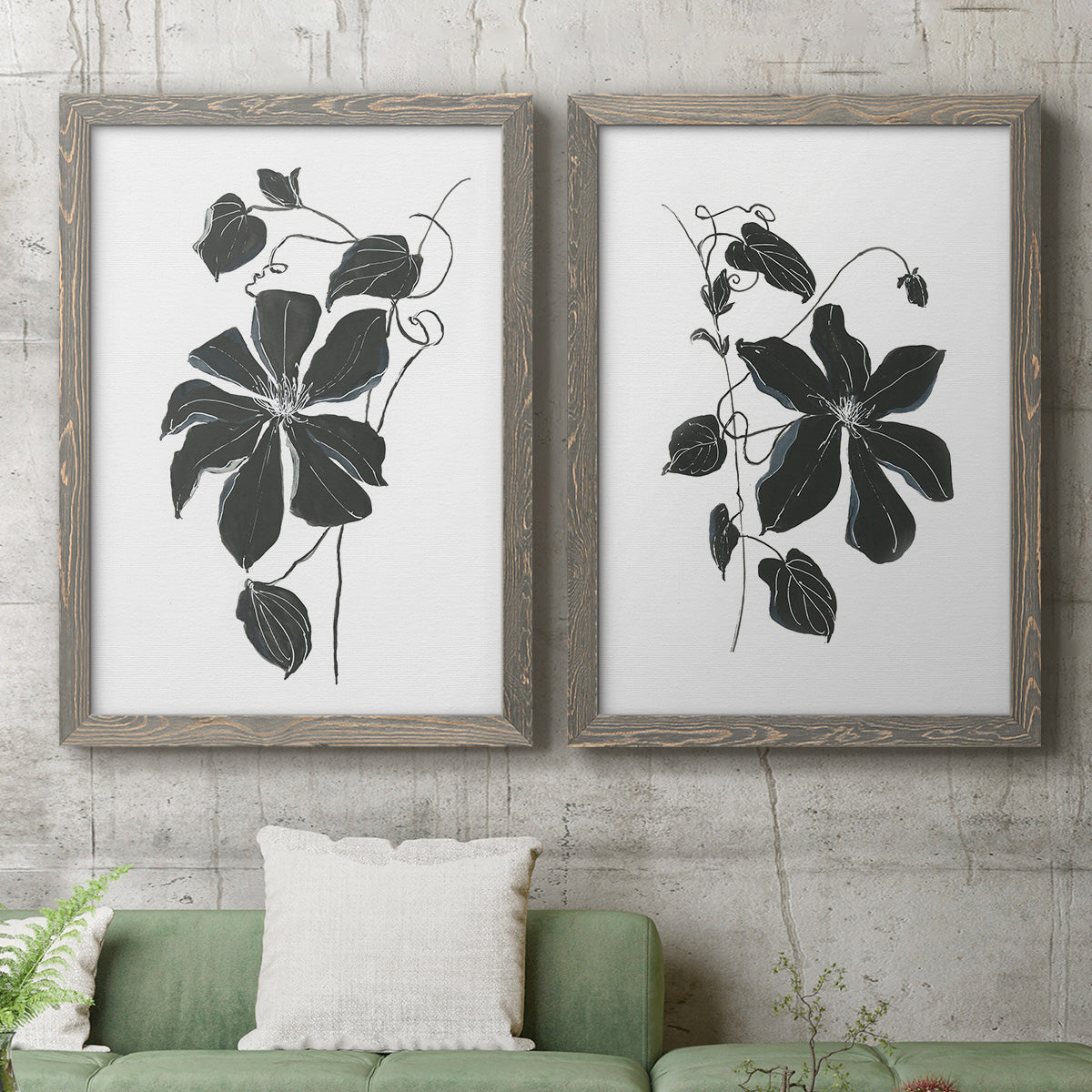 Set of two gray barnwood framed canvas prints depicting a coordinated art pair of black leafy vine silhouettes rendered as minimalist botanical prints above a sofa in a modern living room.