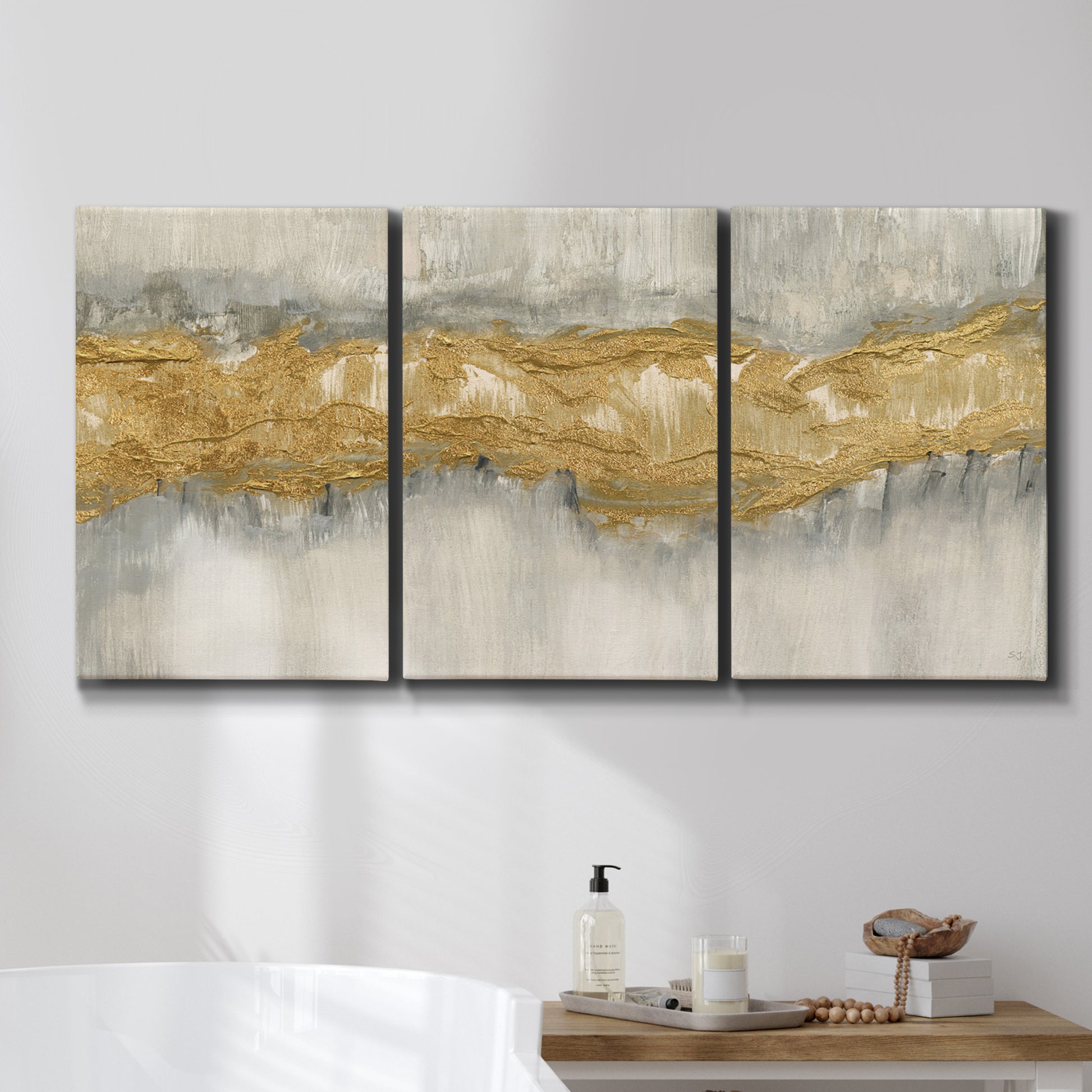 Three-panel canvas wall art featuring flowing abstract golden tones, displayed in a bathroom above a bathtub.