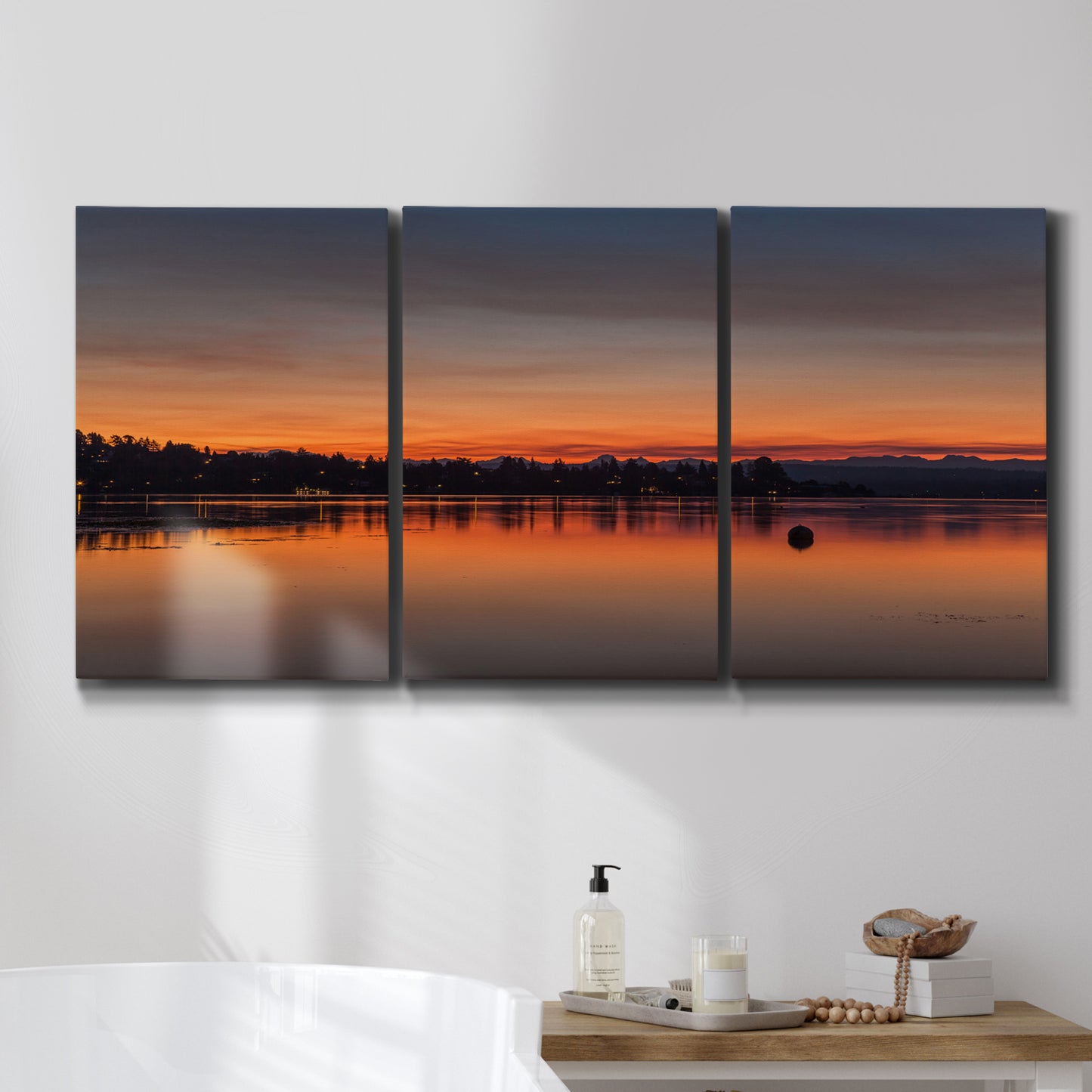 Three-panel canvas wall art featuring glowing sunset over water, displayed in a bathroom above a bathtub.