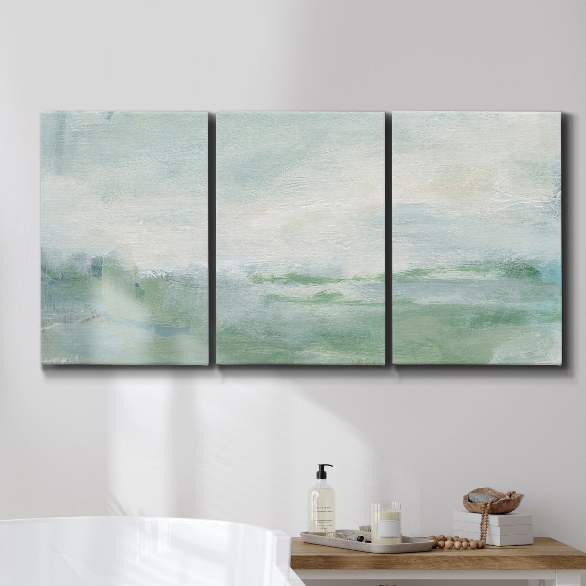 Three-panel canvas wall art featuring soft abstract coastal tones, displayed in a bathroom above a bathtub.