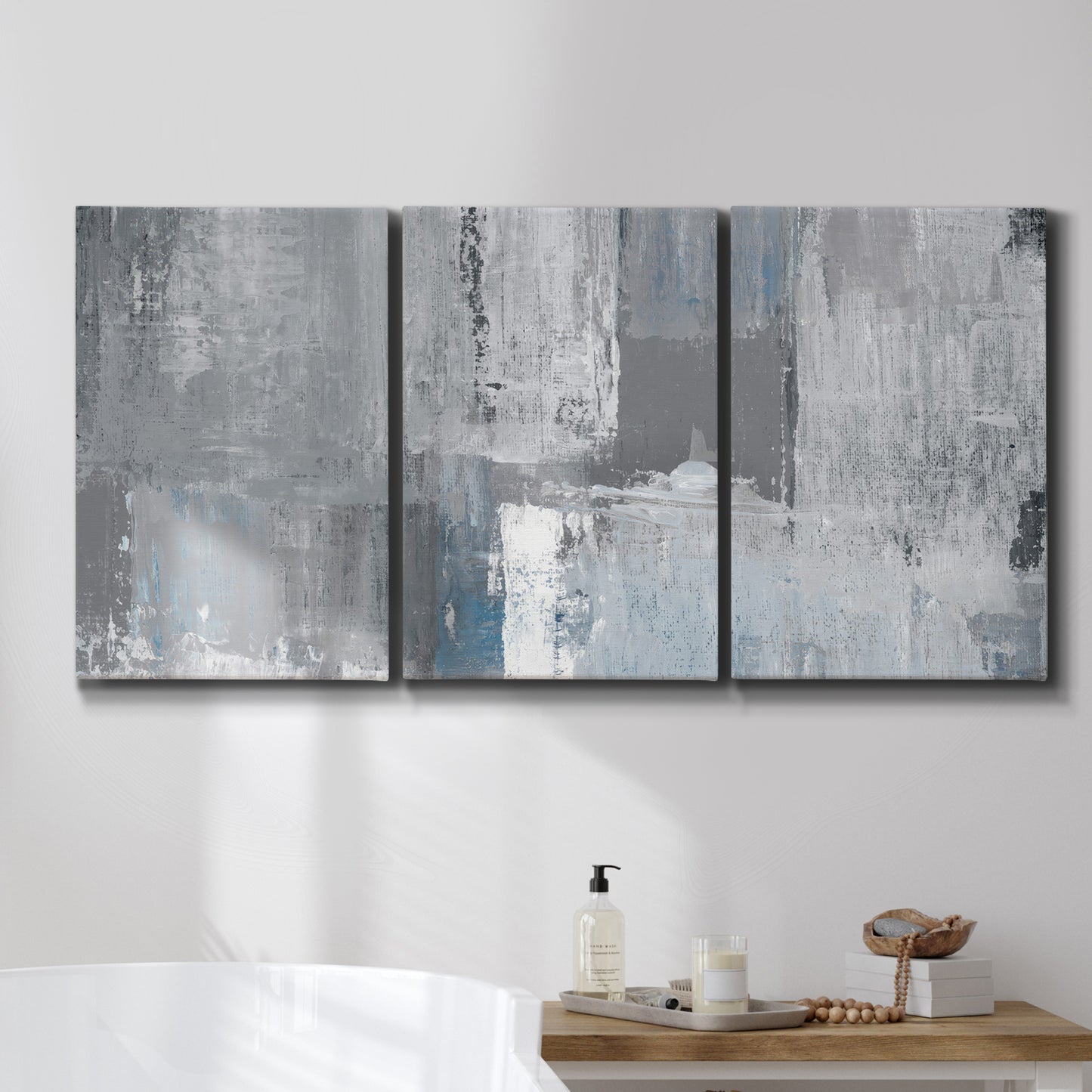Three-panel canvas wall art featuring cool toned industrial abstract blues, displayed in a bathroom above a bathtub.