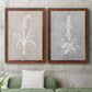 Set of two maple barnwood framed canvas prints depicting a coordinated art pair of white botanical silhouettes on softly weathered neutral backgrounds rendered as rustic minimalist botanical prints above a sofa in a modern living room.