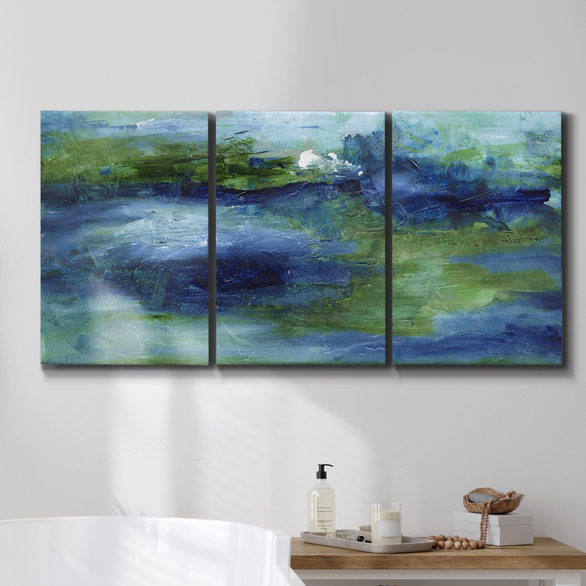 Three-panel canvas wall art featuring flowing blue abstract watercolor, displayed in a bathroom above a bathtub.