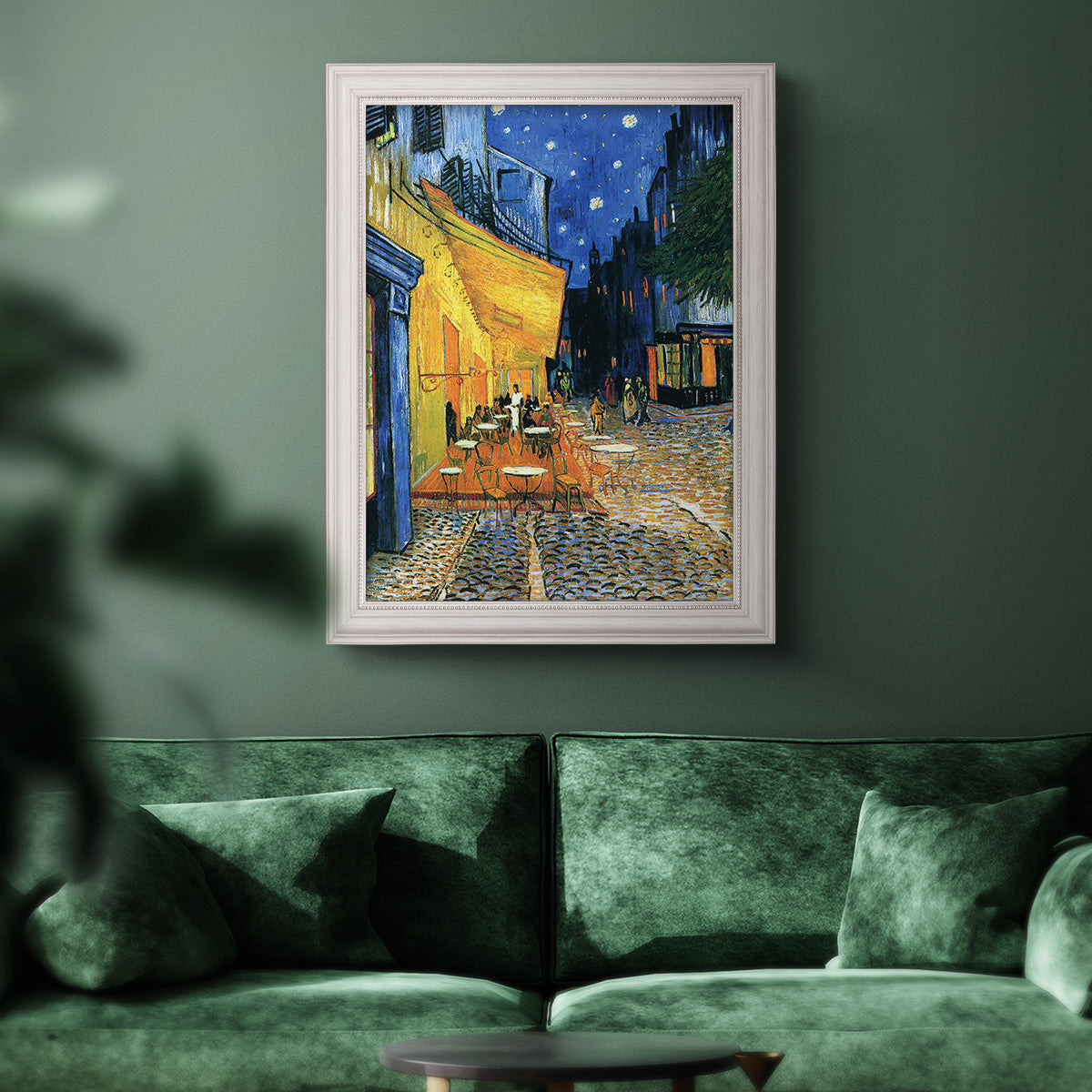 Impressionist night café street scene by Vincent van Gogh in an ornate weathered white frame displayed in a dark-toned interior setting.