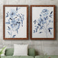 Set of two maple barnwood framed canvas prints depicting a coordinated art pair of loose blue flowers and leafy branches rendered as expressive watercolor botanical paintings above a sofa in a modern living room.