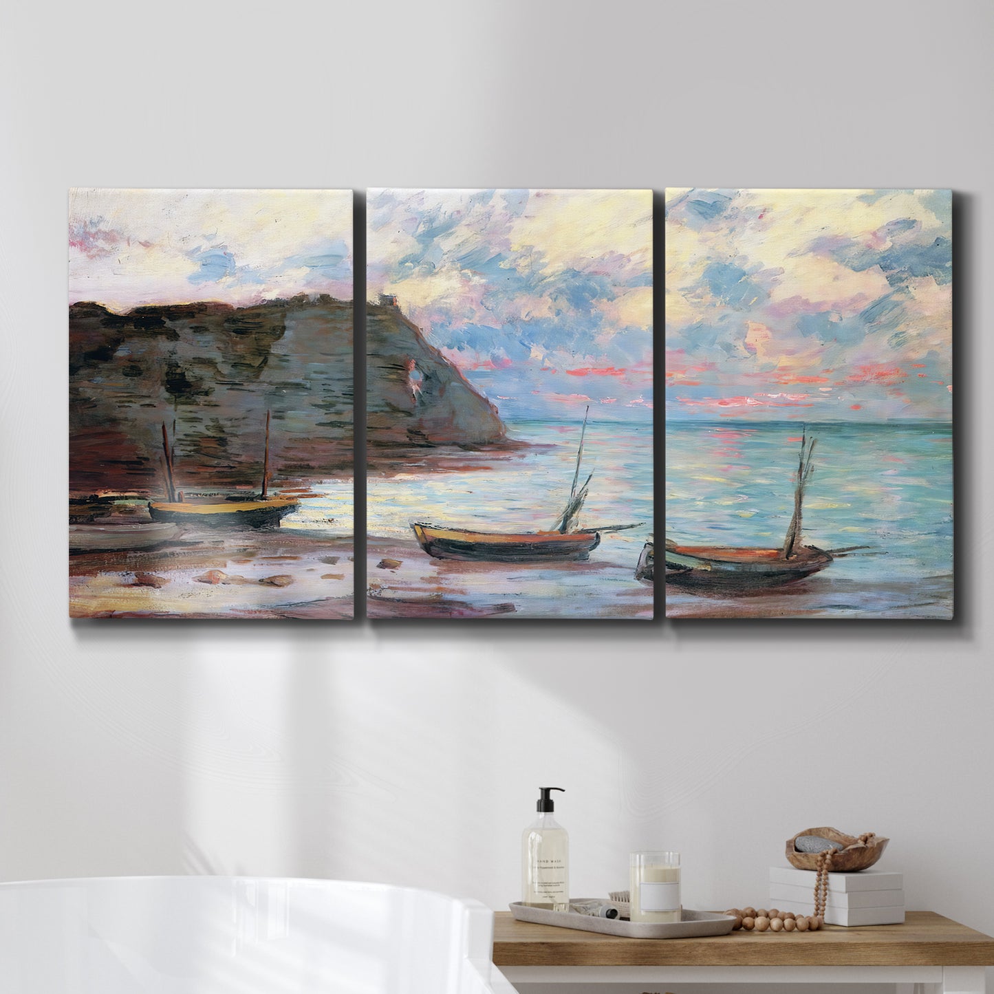 Three-panel canvas wall art featuring golden coastal sunset with cliffs, displayed in a bathroom above a bathtub.