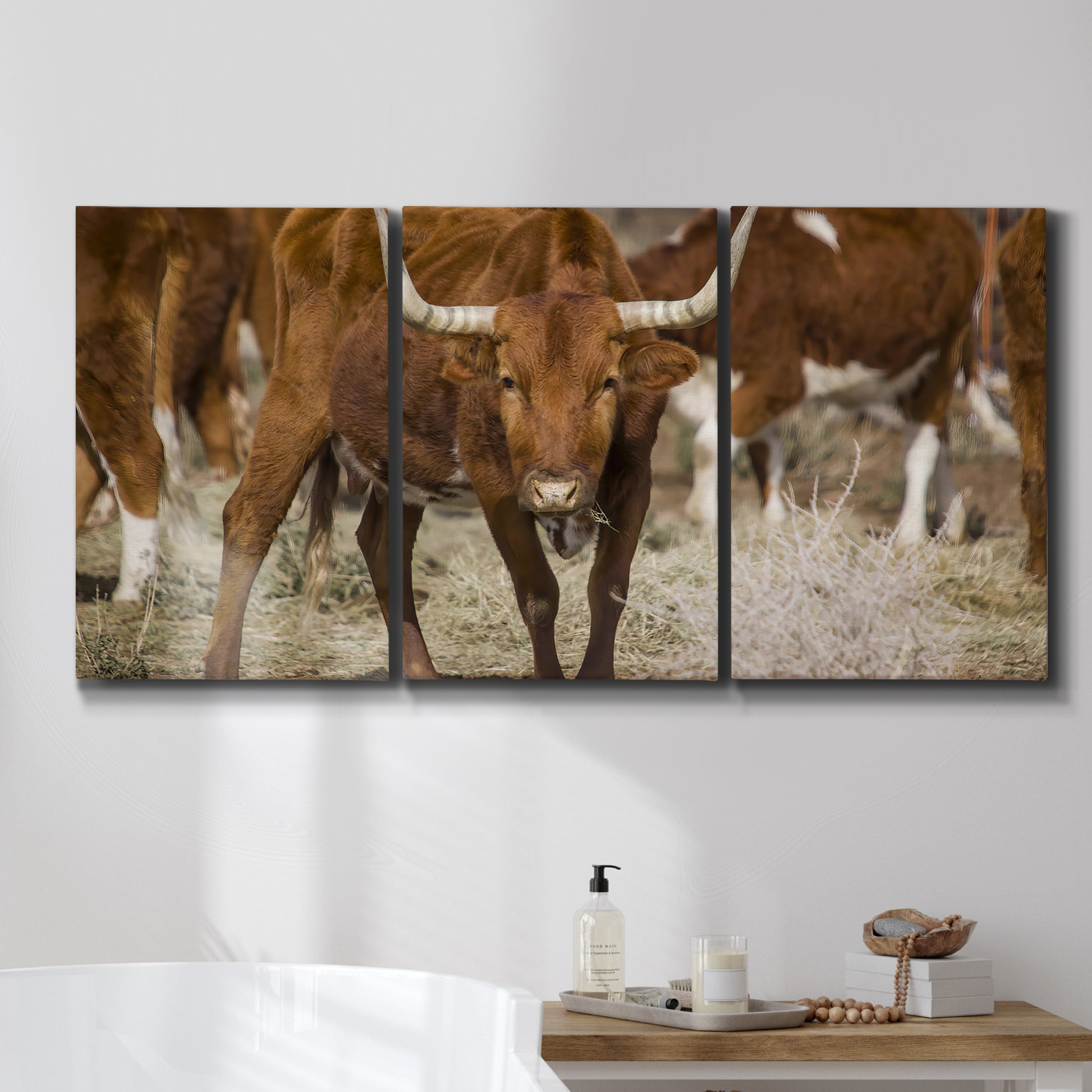 Three-panel canvas wall art featuring longhorn cattle standing together, displayed in a bathroom above a bathtub.
