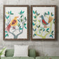 Set of two walnut barnwood framed canvas prints depicting a coordinated art pair of stylized colorful birds perched among leafy branches rendered as modern folk-art bird illustrations above a sofa in a modern living room.