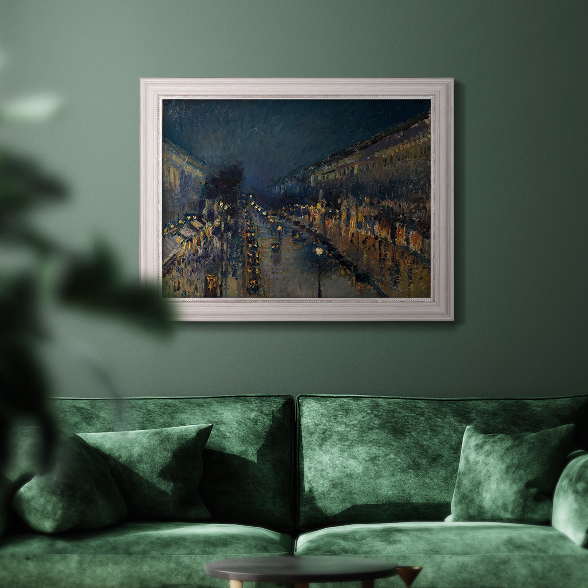 Impressionist nighttime Paris street scene by Camille Pissarro in an ornate weathered white frame displayed in a dark-toned interior setting.