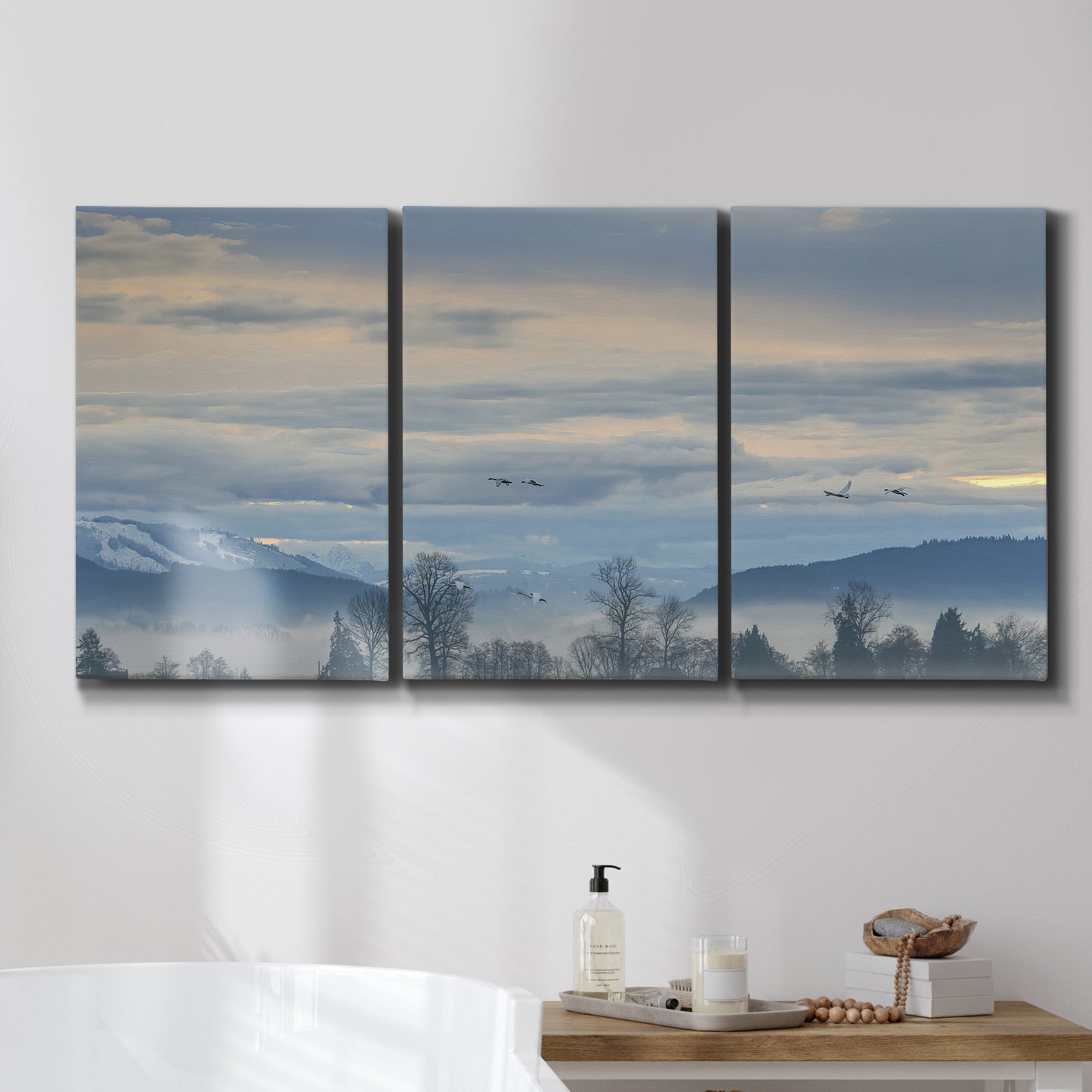 Three-panel canvas wall art featuring misty horizon over quiet landscape, displayed in a bathroom above a bathtub.